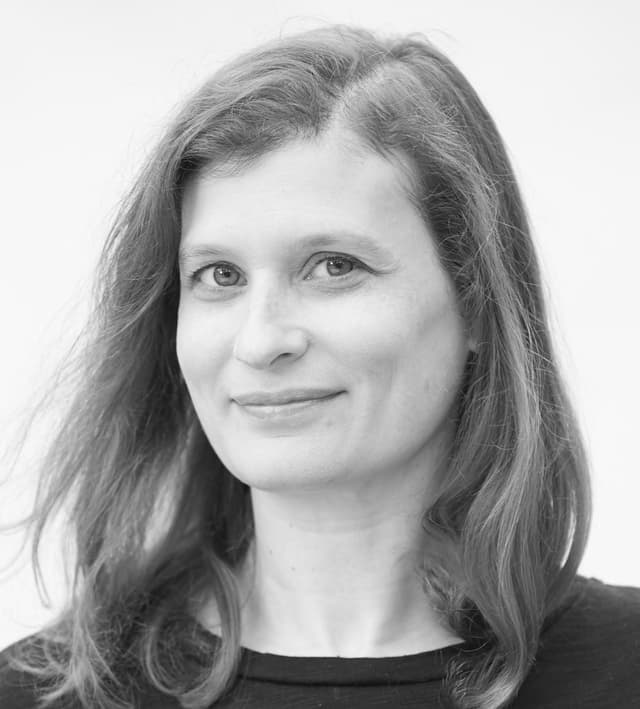 A black and white portrait of a woman with long, wavy hair and a warm, friendly expression on her face.