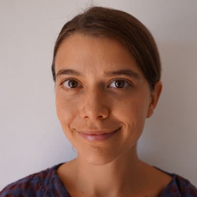 A smiling woman with dark hair and a friendly expression is the focus of the image, set against a plain white background.