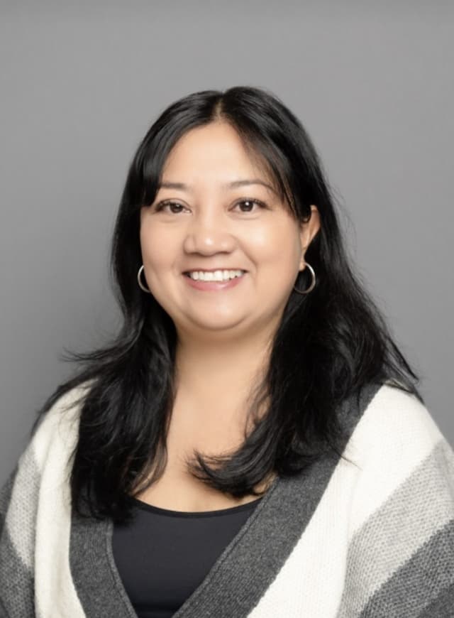 The image shows a smiling woman with long dark hair wearing a white and gray sweater against a gray background.