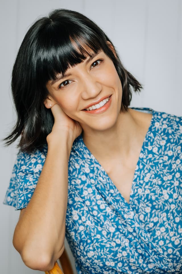A smiling woman with short dark hair wearing a blue floral blouse against a plain light background.